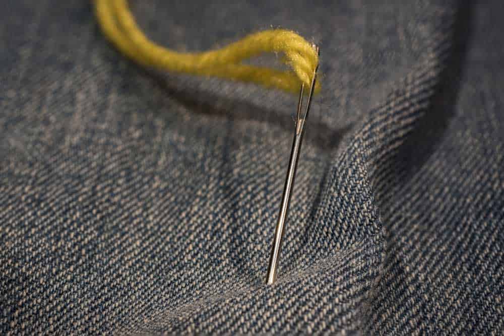 A yellow thread, a needle, and a jeans fabric